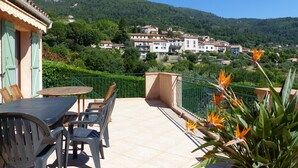 Une terrasse avec une table et des chaises, donnant sur un village perché sur une colline, avec ses bâtiments.