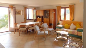 Un salon spacieux comprenant un coin repas, un canapé avec des coussins, une table basse et un coin cuisine avec des placards.