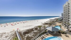 Blick auf einen Strand mit einem Hotel, einem Schwimmbecken und Strandstühlen.