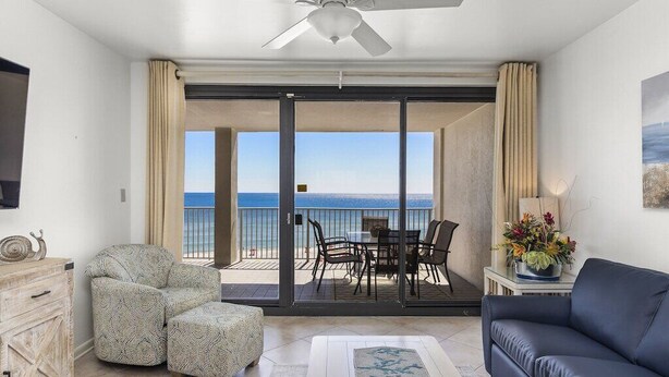 Ein Wohnzimmer mit Sofa, Sessel und Hocker, einem Esstisch mit Stühlen sowie einem Balkon mit Meerblick.