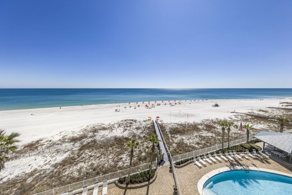 Un resort en la playa con piscina, sillas de playa y una vista despejada del océano.