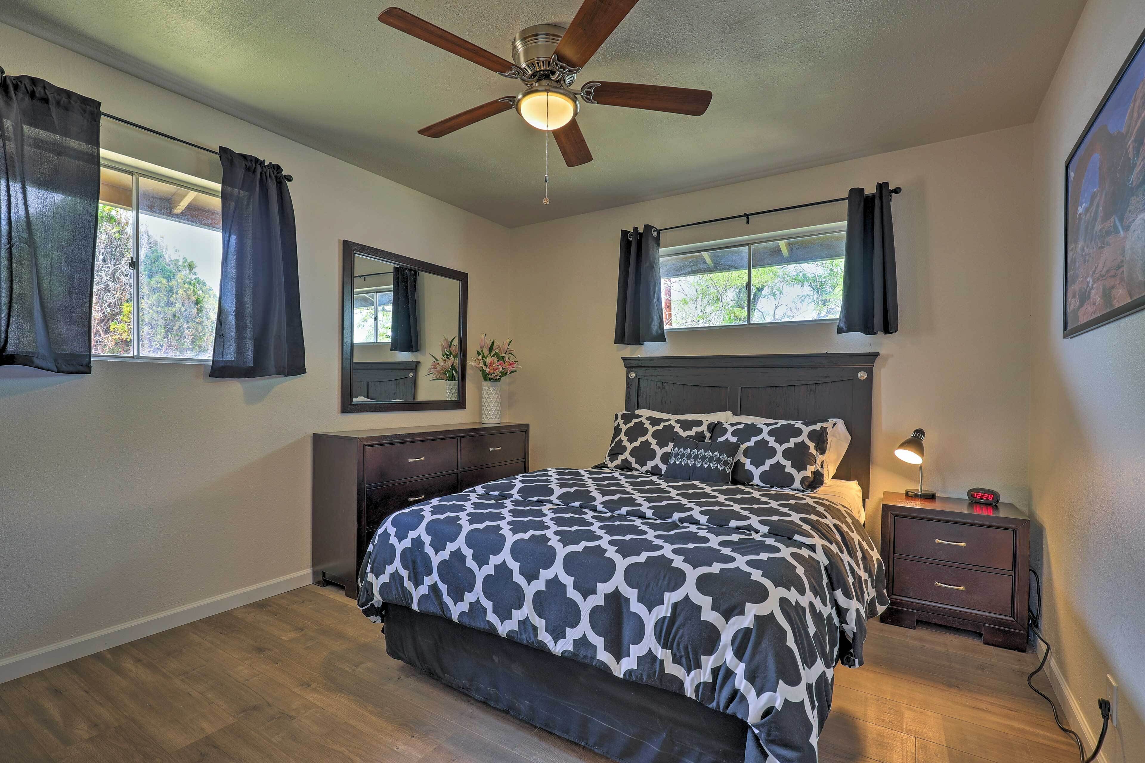 A bedroom with a bed, a nightstand, a mirror, a ceiling fan, and a window with curtains.