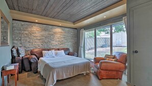 Een slaapkamer met een stenen muur, een groot bed, een lederen fauteuil en uitzicht op het omliggende landschap.