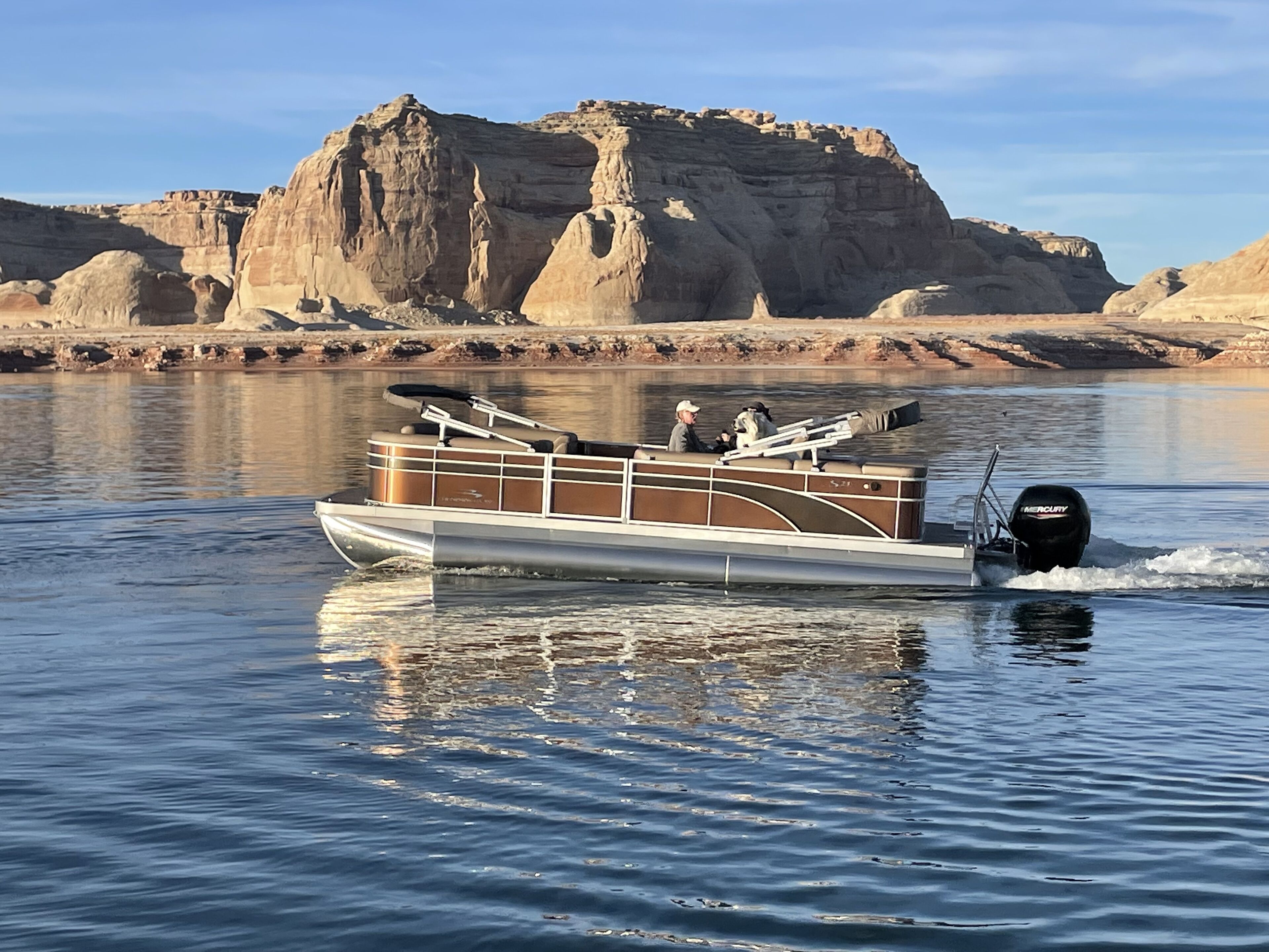 Un bateau à moteur doté d’une cabine et d’un espace salon, naviguant sur une eau calme, avec un paysage rocheux en arrière-plan.