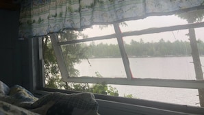 Huone, jossa on ikkuna, josta avautuu näkymä järvelle. Huoneessa on ruutukuviollinen päiväpeite ja luontoaihekuvioitu verho.