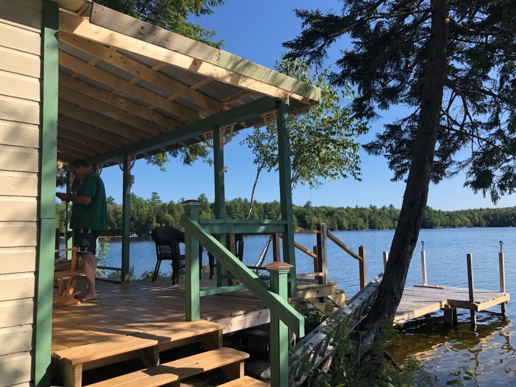 A wooden deck with steps leading to a covered area, overlooking a lake.