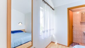 A bedroom with a bed, a mirror, a window with curtains, and a bathroom visible through an open door. - Summer Dream - One Bedroom Apartment with Sea View (Privlaka)
