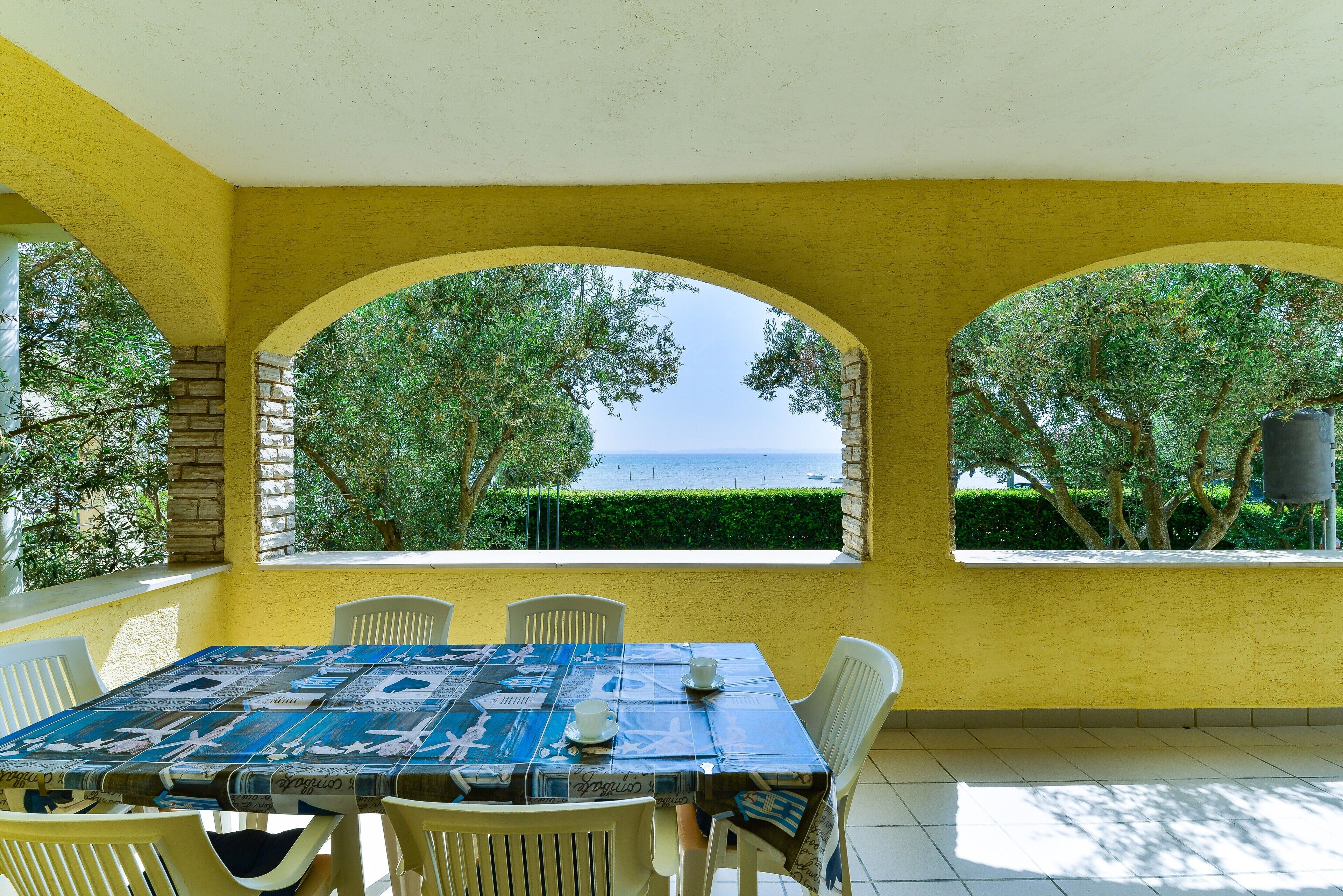 A dining area with a table set for two, yellow walls, and a view of the sea through arched windows.