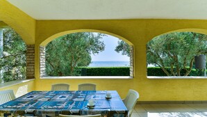 Un comedor con una mesa dispuesta para dos, paredes amarillas y vistas al mar a través de ventanas arqueadas.