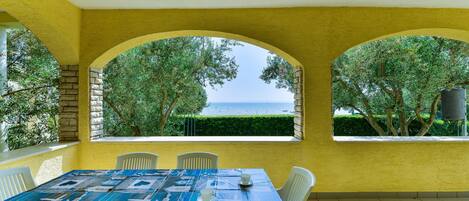 Un coin repas avec une table dressée pour deux personnes, des murs jaunes et une vue sur la mer à travers des fenêtres en arc de cercle.