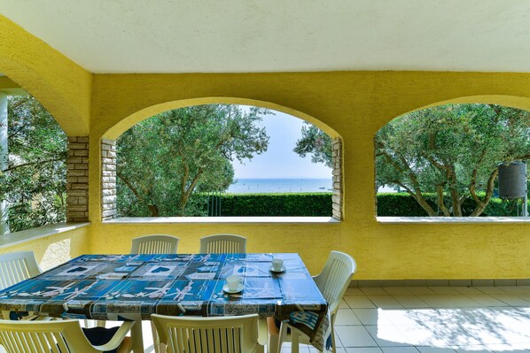 A dining area with a table set for two, yellow walls, and a view of the sea through arched windows.