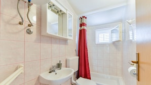 A bathroom with a white sink, toilet, and bathtub. There is a window with a red curtain, and a mirror above the sink. - Summer Dream - One Bedroom Apartment with Balcony and Sea View (Privlaka)
