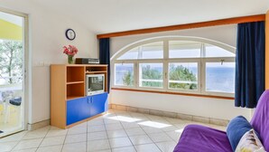 A room with a large window overlooking the sea, a wooden cabinet, and a purple sofa. - Summer Dream - One Bedroom Apartment with Balcony and Sea View (Privlaka)