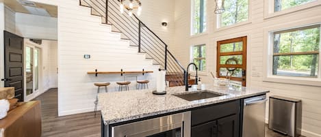 Une cuisine moderne dotée d’un plan de travail en granit, d’appareils électroménagers en acier inoxydable et d’un escalier en bois.