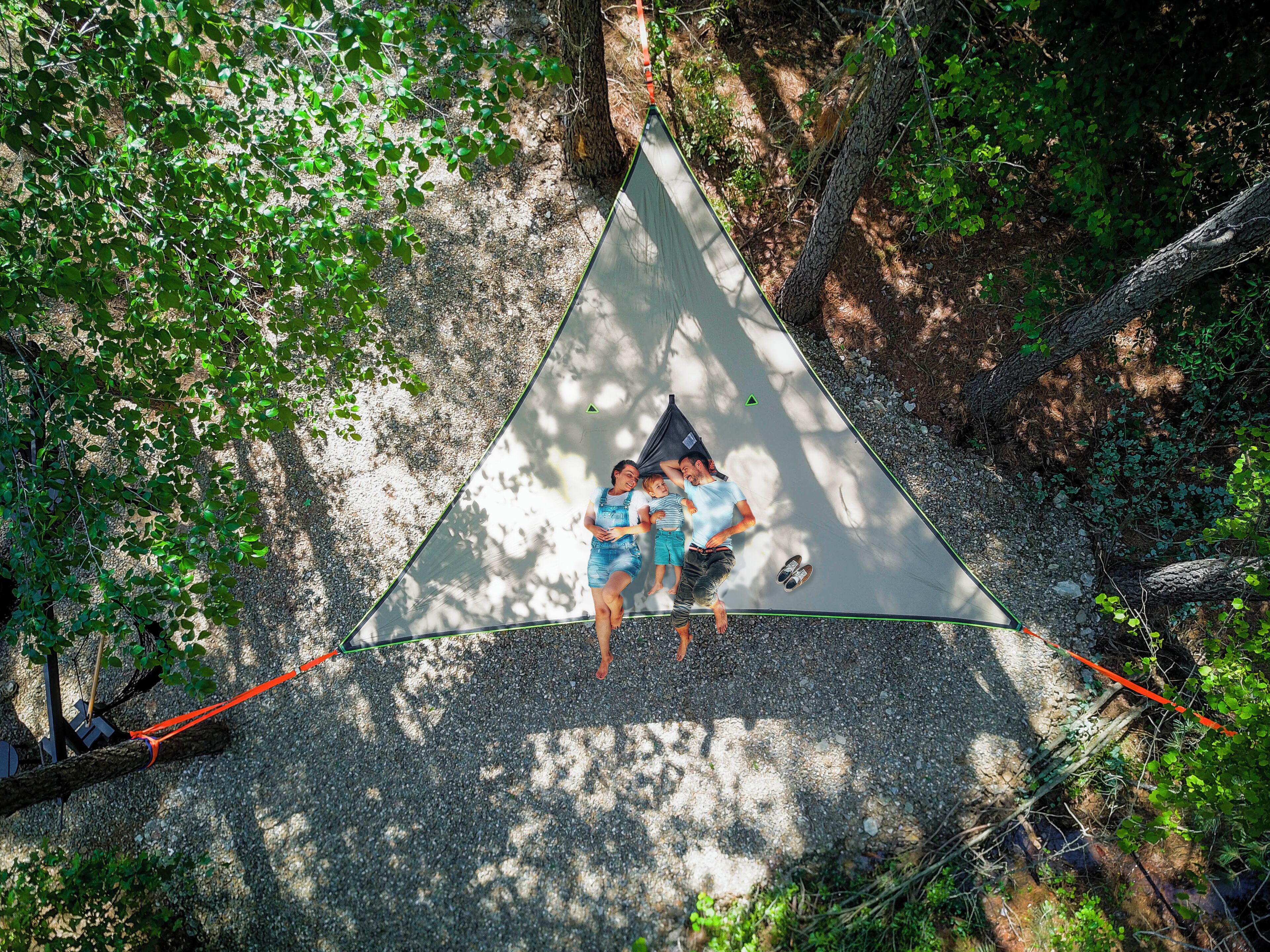 A triangular tent set up in a forested area with trees and gravel ground.