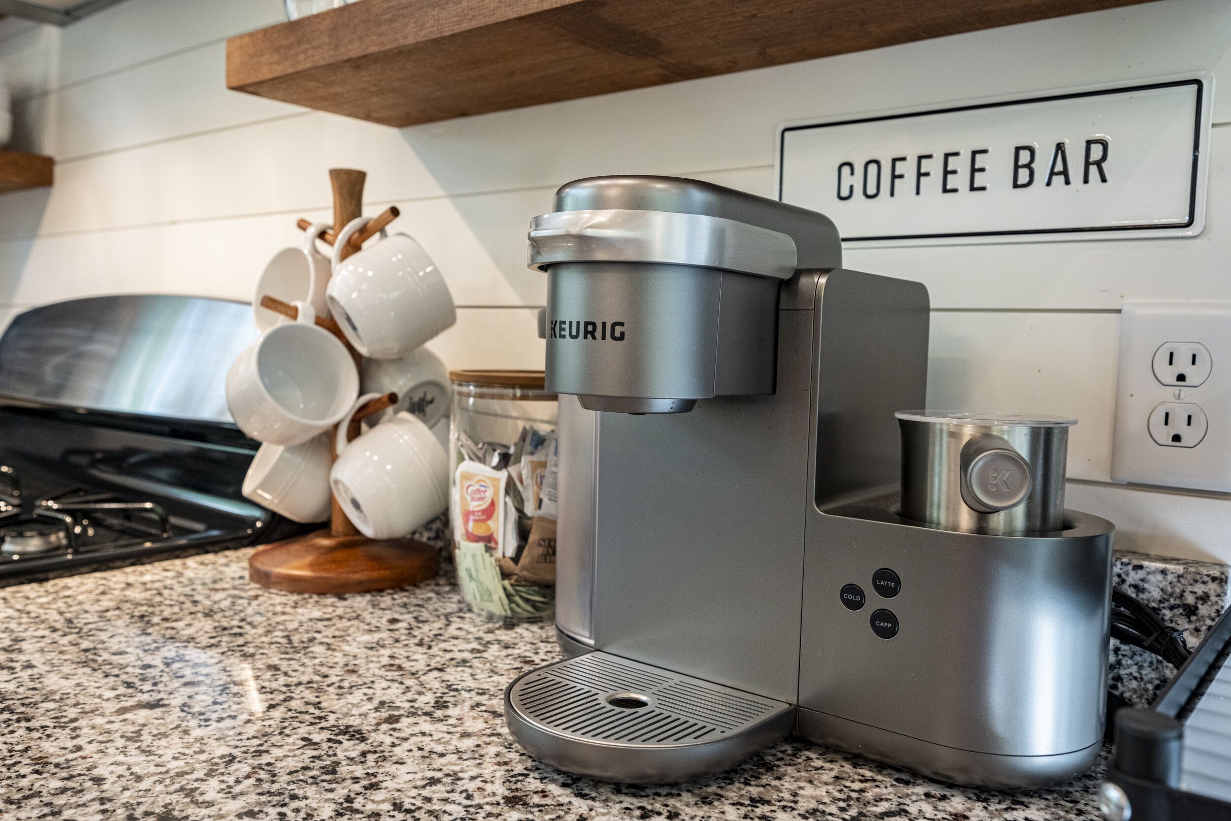 Una cafetera sobre una encimera de cocina con un letrero que dice 'COFFEE BAR' encima.