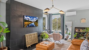 Un salon moderne doté d’un grand téléviseur, de sièges confortables et offrant une vue sur l’extérieur.