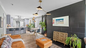 Un salon moderne avec un canapé, une table basse et un coin repas comprenant une table et des chaises. On aperçoit au fond une cuisine avec un comptoir et des placards.