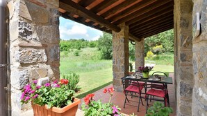A stone-built outdoor patio with a table and chairs, surrounded by potted plants and a view of a grassy landscape. - Villa Nocciola "Lovely cottage in the nature" (Roccalbegna)