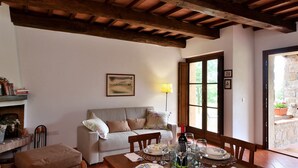 A cozy living room with a sofa, dining table set for two, and a large window with a view of greenery. - Villa Nocciola "Lovely cottage in the nature" (Roccalbegna)
