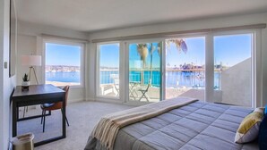 Un dormitorio con una cama grande, un escritorio y vistas a una piscina y una playa.