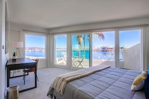 Une chambre avec un grand lit, un bureau et une vue sur une piscine et une plage.