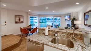 Una cocina moderna con una isla grande, pileta de acero inoxidable y un comedor con sillas rojas.
