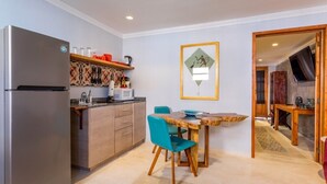 Une cuisine compacte équipée d’un réfrigérateur, d’un four à micro-ondes et de meubles de rangement en bois. Elle comprend également un coin repas avec une table et des chaises.