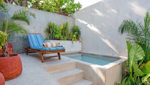 Un espace piscine agrémenté d’une chaise longue en bois, de quelques marches menant à la piscine et de divers plantes en pot.