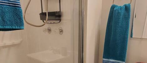 A shower with a glass door, a blue towel, and a small basket with a star decoration.