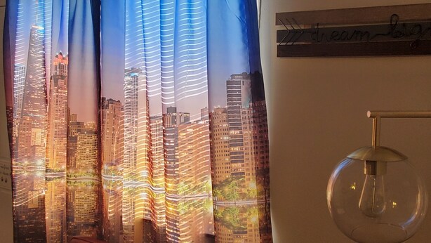Een gordijn met een stadsgezicht, een bordje aan de muur met de tekst 'dream' en een glazen lamp.
