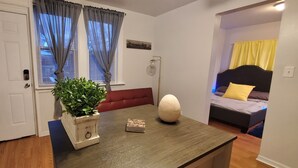 Een kamer met een houten tafel, een potplant, een rode bank en een bed met geel en bruin bedkussen.
