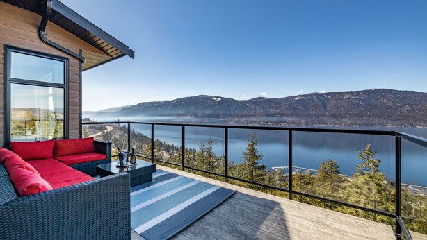 Un balcón con vista a un lago y montañas, amueblado con un sofá y una mesa.