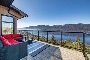 A balcony with a view of a lake and mountains, furnished with a sofa and a table.