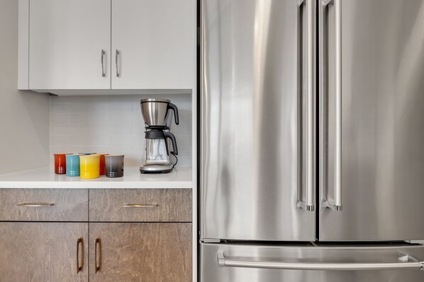 A kitchen with white cabinets, a stainless steel refrigerator, and a coffee maker on the counter.
