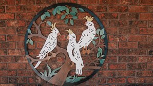 A wooden table with a metal bird decoration on a brick wall. - Donald Motor Lodge (Donald)