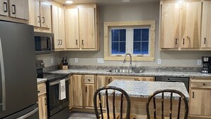 A modern kitchen with wooden cabinets, a stainless steel refrigerator, a granite countertop, and two rustic wooden chairs. - Newly Renovated Cabin -dog friendly (Tomahawk)