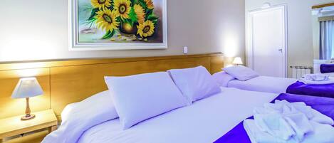 A hotel room with a large bed, a nightstand with a lamp, and a painting of sunflowers on the wall.