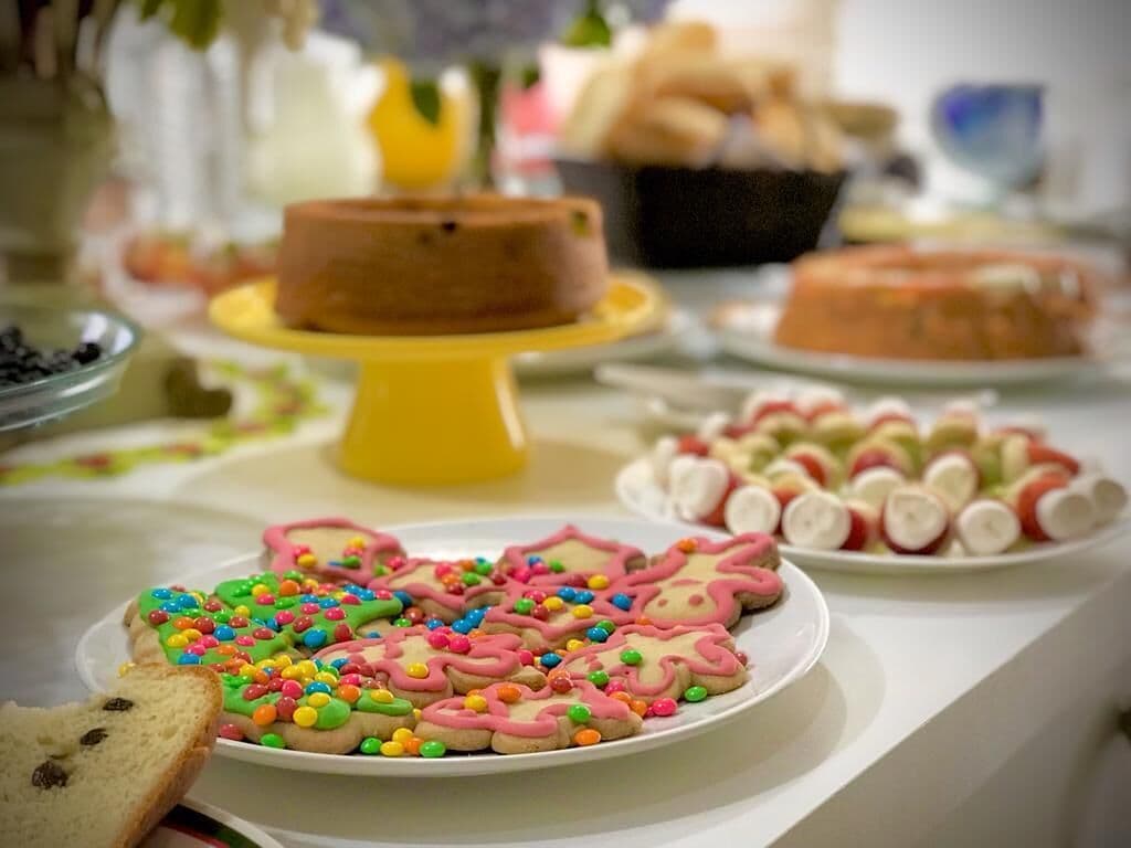 A table with various food items, including decorated cookies and a cake on a yellow stand.