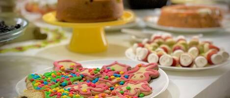 A table with various food items, including decorated cookies and a cake on a yellow stand.