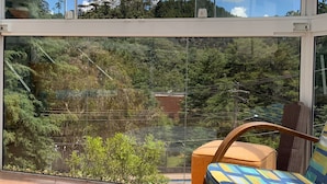 Ein Balkon mit Glasbrüstung, einem Holzstuhl und einem gemusterten Kissen.