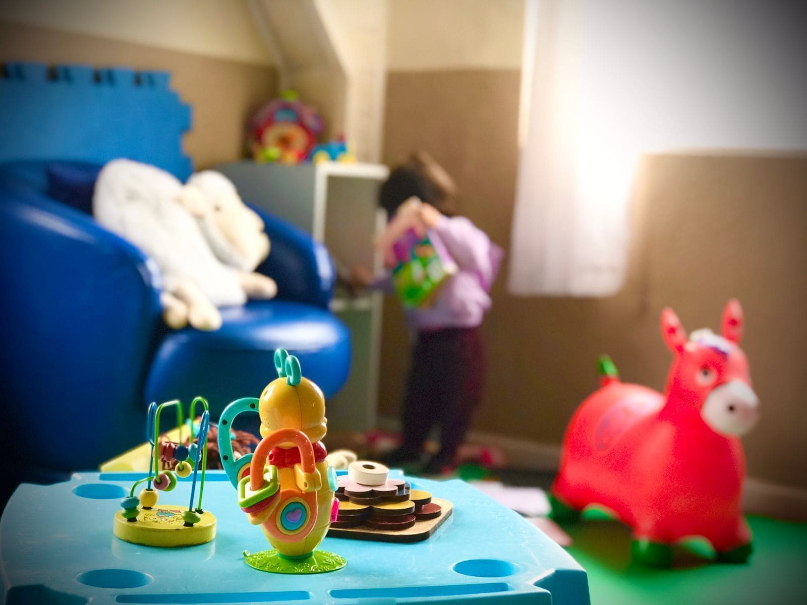 A room with a blue sofa, a child playing with toys, and a red toy elephant.
