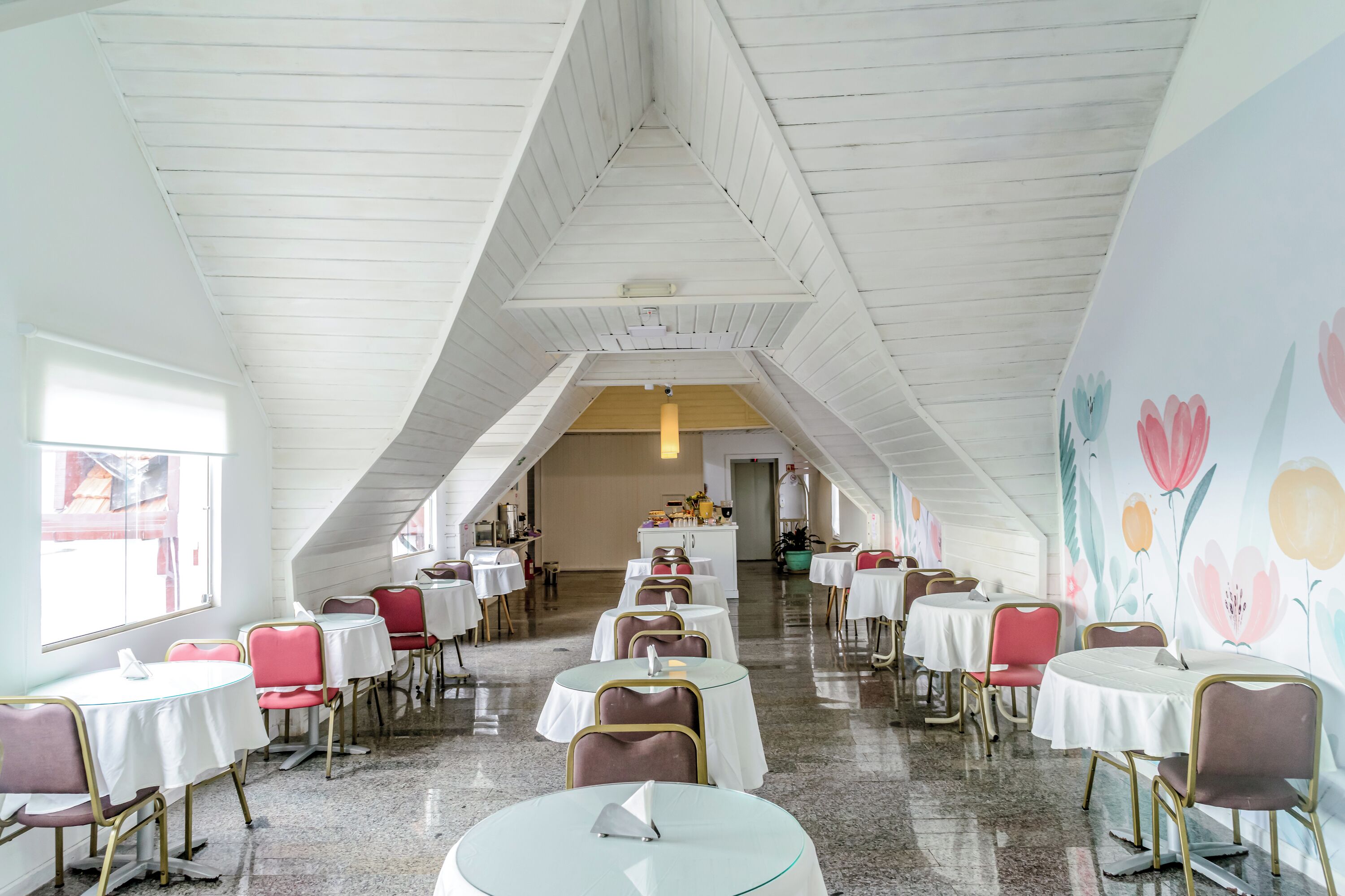 A restaurant with white wooden ceiling, round tables, and red chairs.