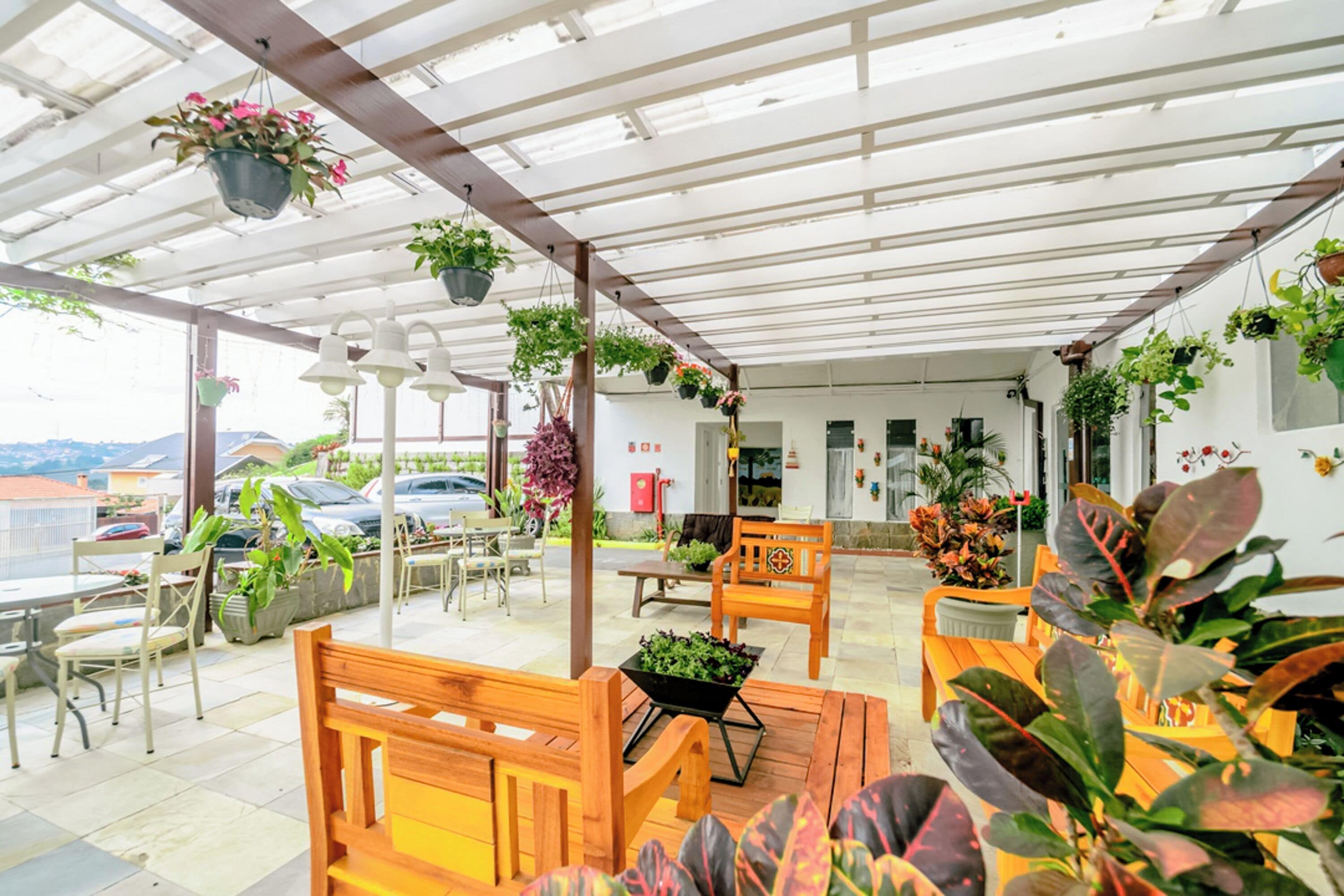 Un espace extérieur aménagé, abrité et doté de bancs et de tables en bois, entouré de plantes en pot et de suspensions florales.