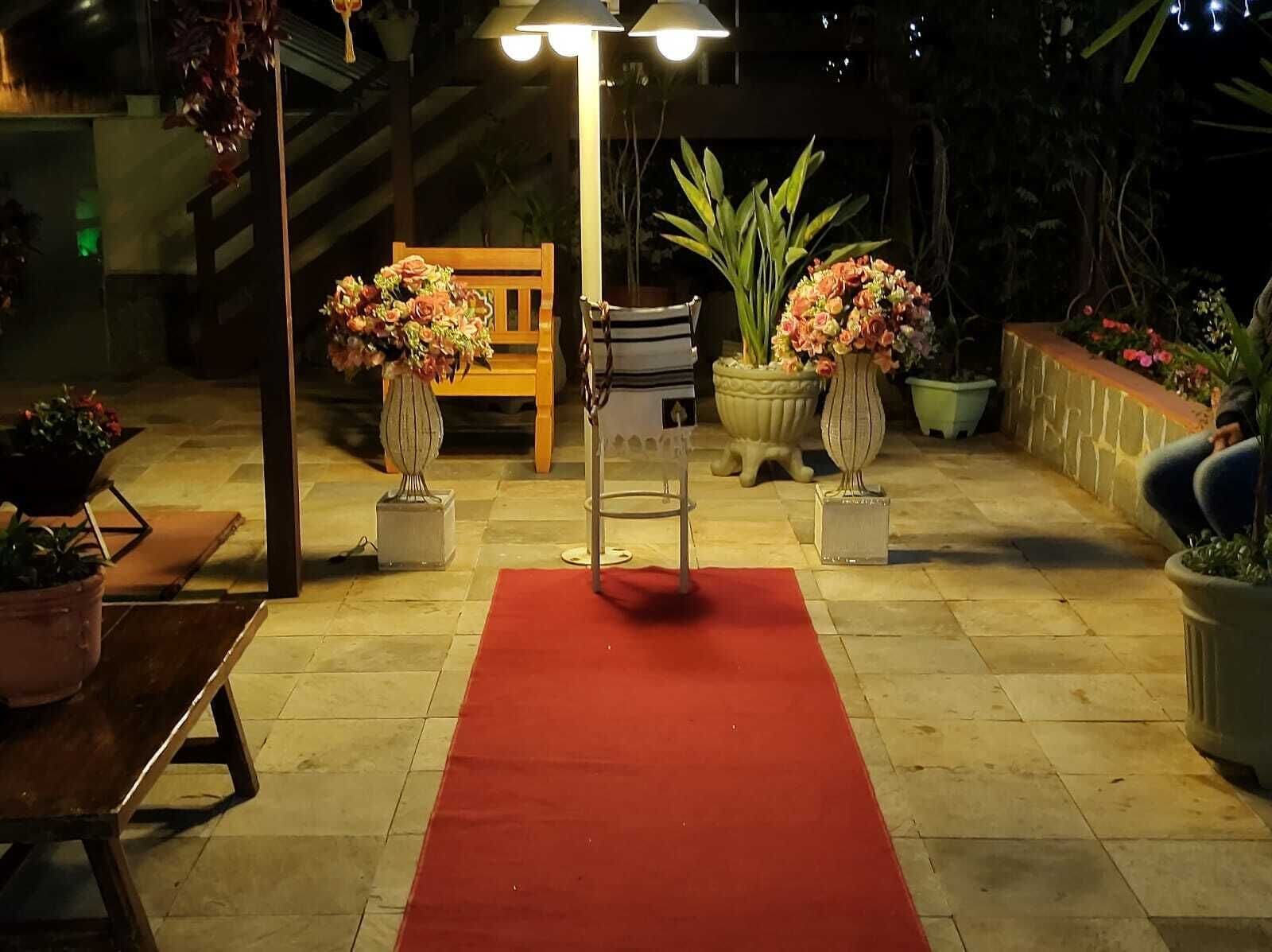 Un espacio al aire libre con una alfombra roja que conduce a un banco, rodeado de plantas en macetas y una escalera.