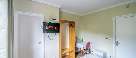 A hotel room with a bed, a desk, a chair, a TV mounted on the wall, and a closet.