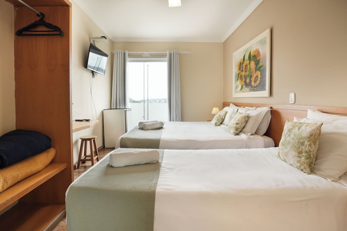 Habitación de hotel con dos camas, televisión, escritorio y ventana con cortinas.