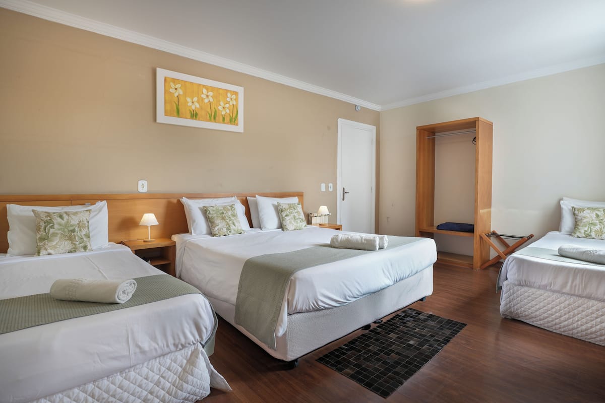Una habitación de hotel con dos camas, un armario de madera, un cuadro en la pared y una pequeña mesa con lámpara.