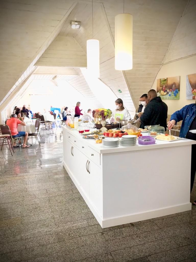 Montaje de bufé con un mostrador blanco, diferentes platillos y personas comiendo.