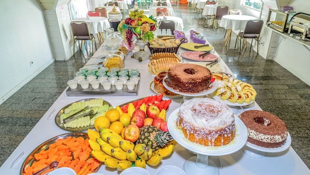 Ein reichhaltiges Buffet mit verschiedenen Früchten, Gebäck und Kuchen in einem geräumigen Raum mit Tischen und Stühlen.